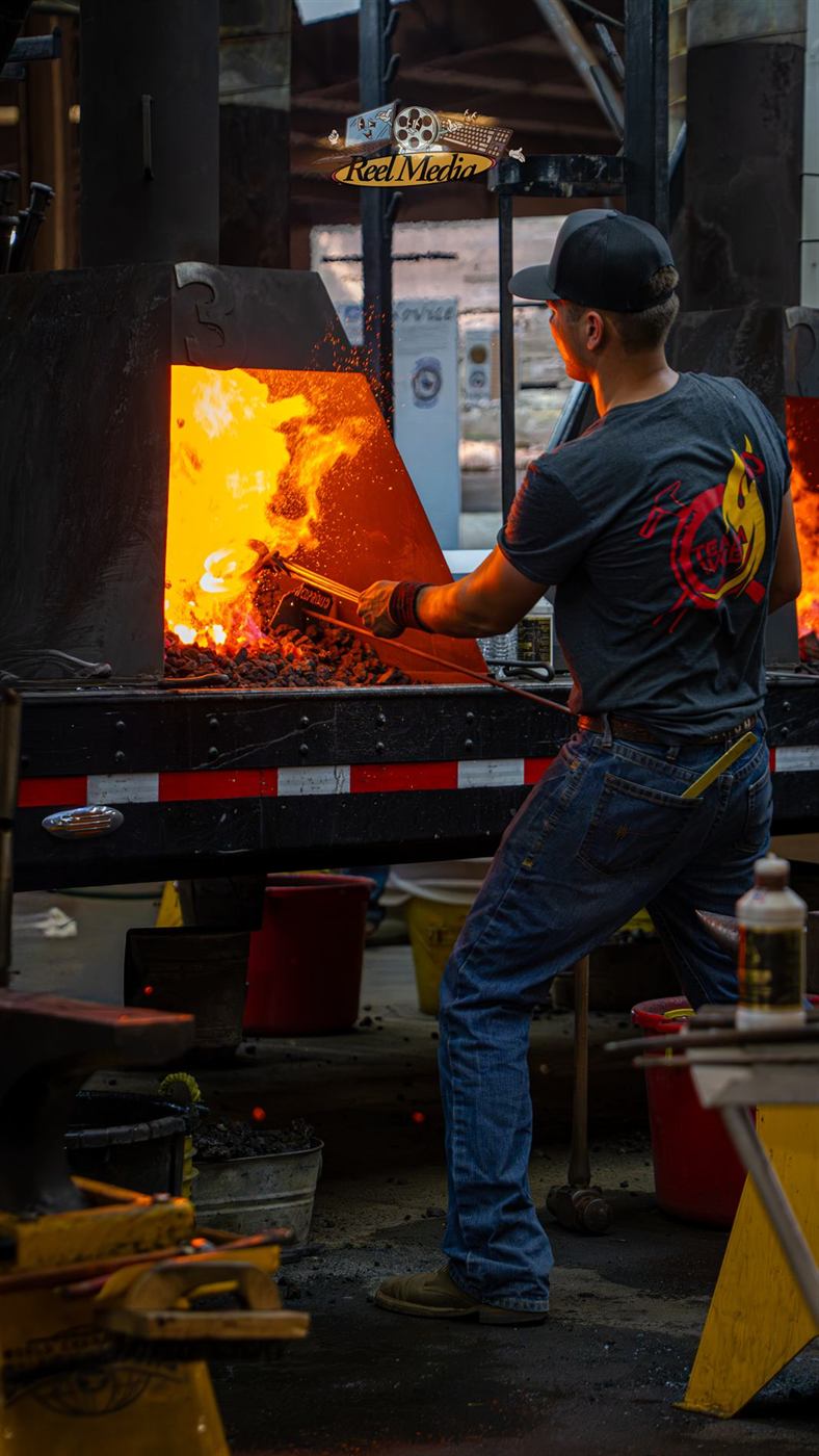 A smith pulling hot iron from the forge with tongs